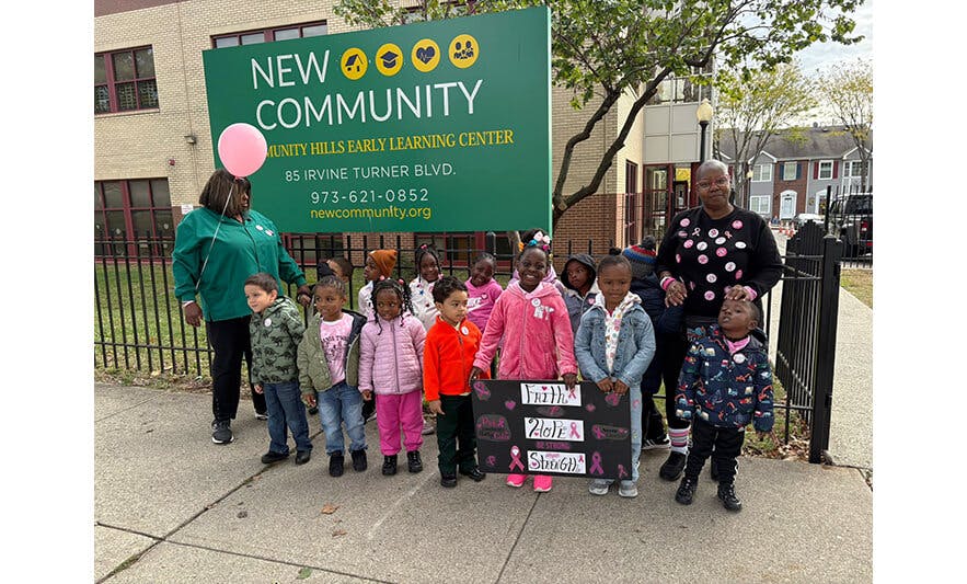People with children holding a sign with text in front of a building