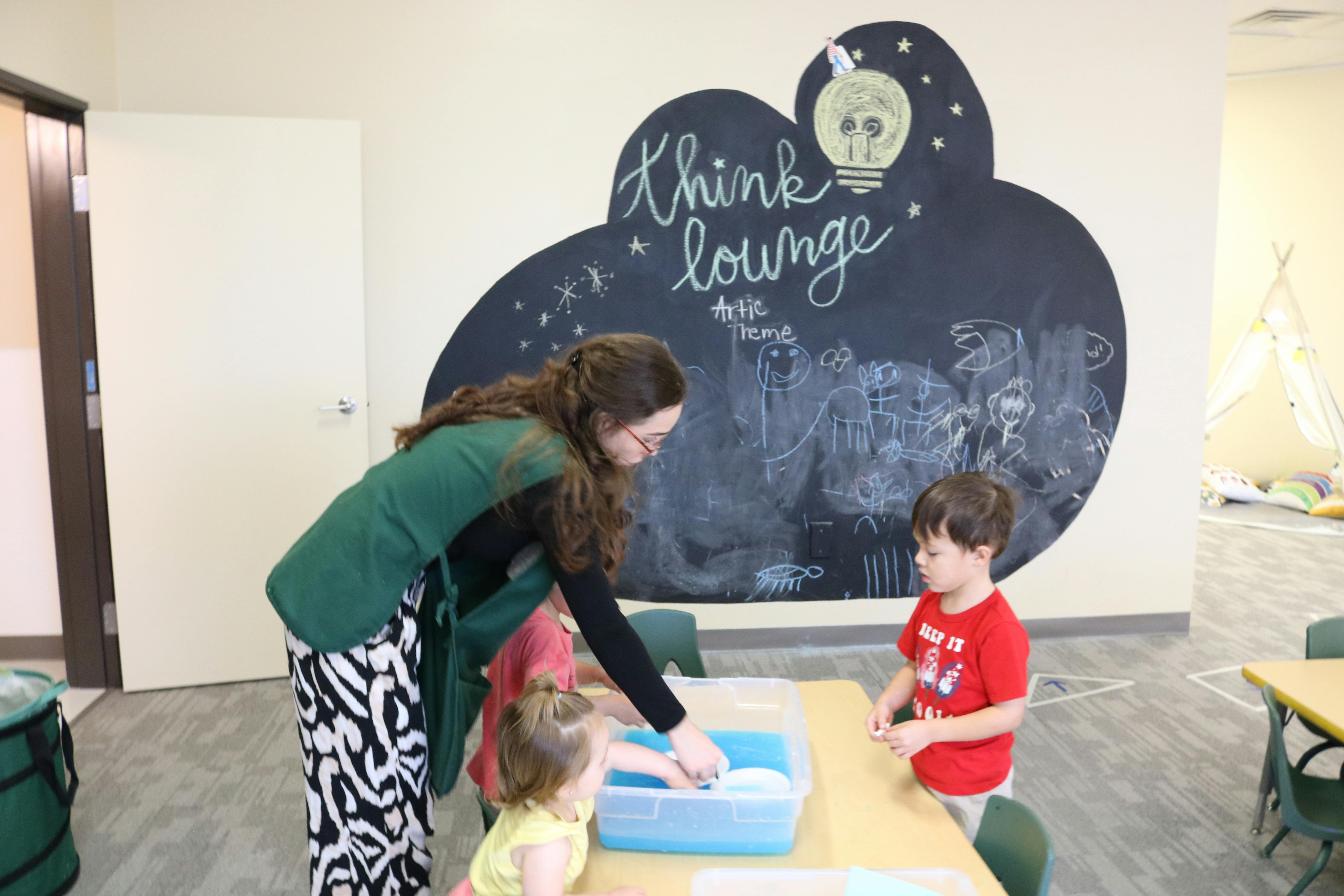 Person and two children interacting with a water table in a bin