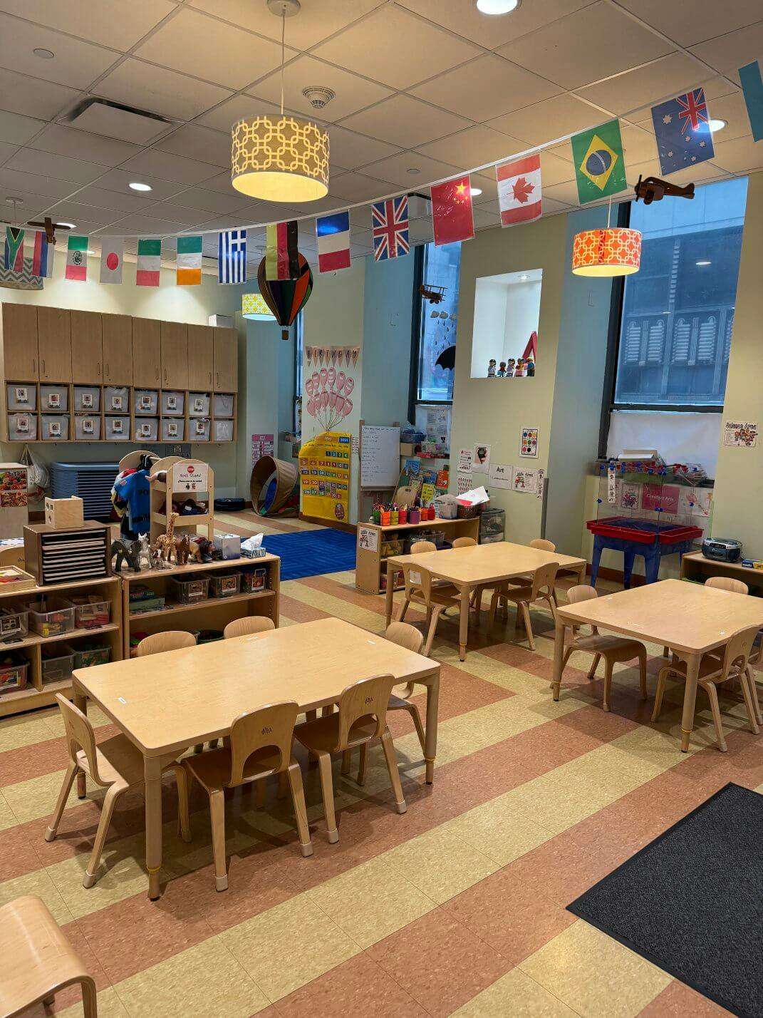 Classroom with small tables and chairs, flags hanging from the ceiling