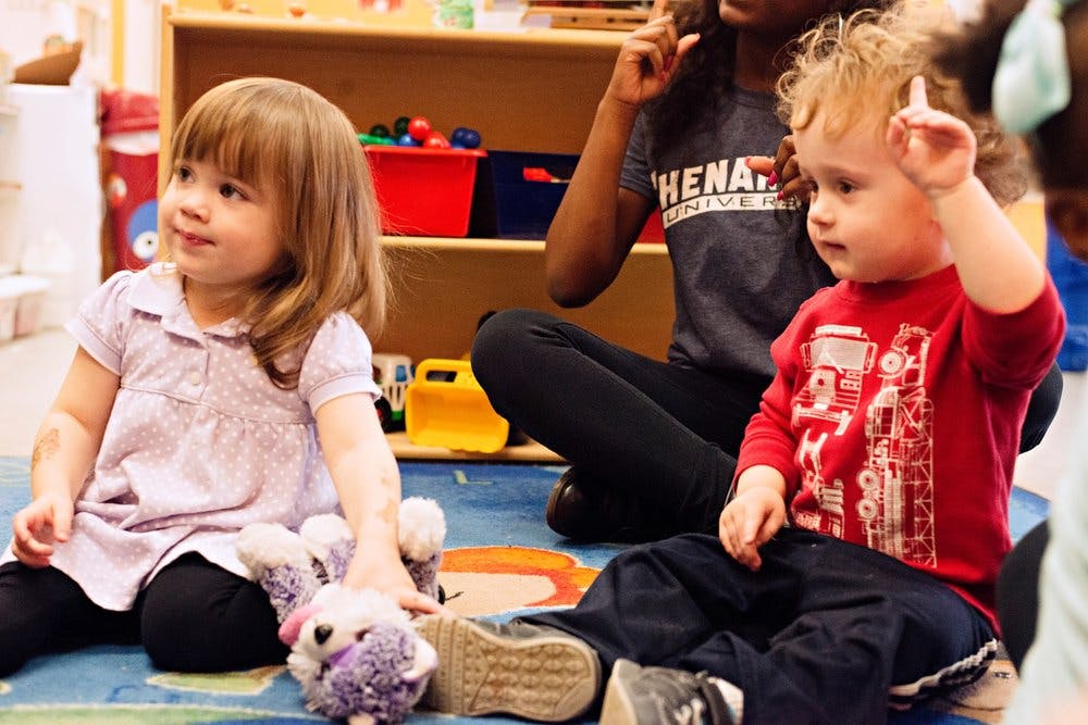 Two children sitting on the floor with an adult in the background