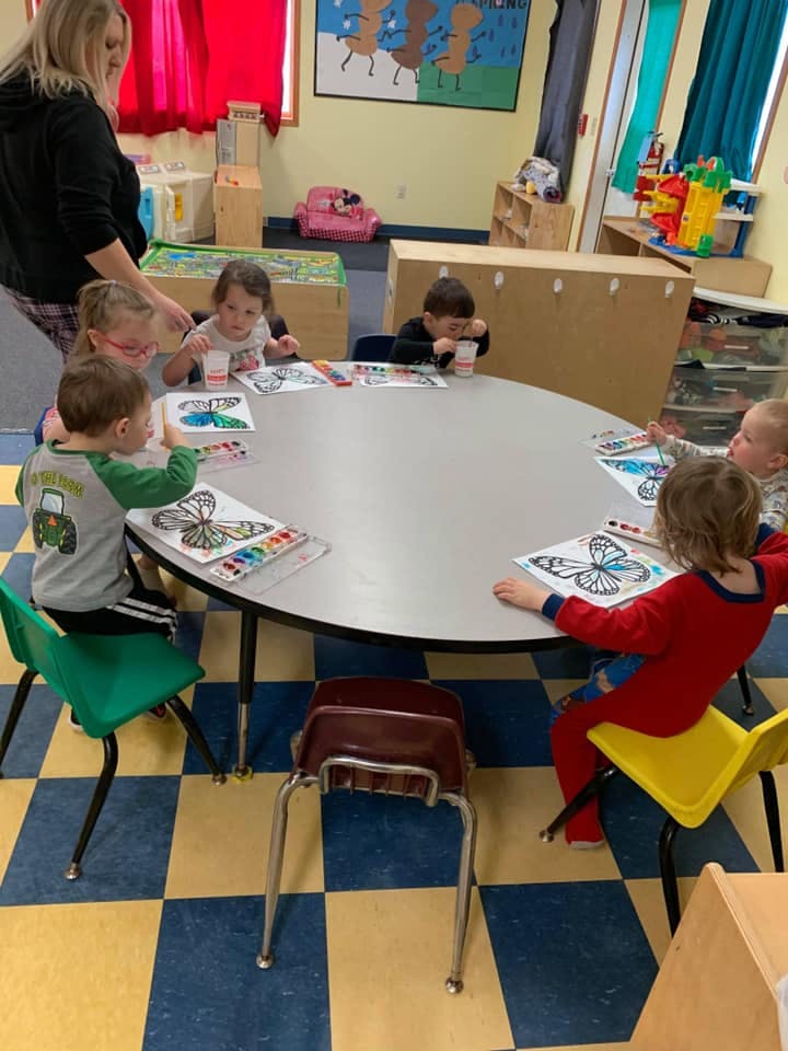 Adult and multiple children coloring at a round table in a classroom