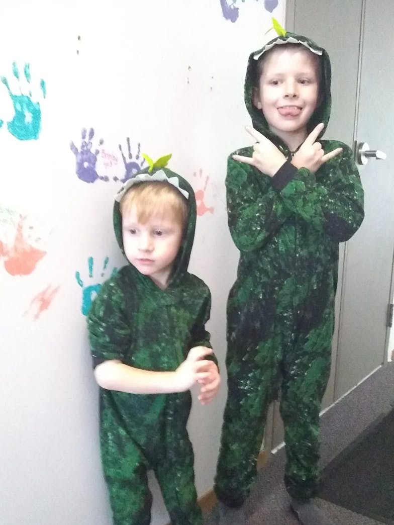 Two children in green hooded dinosaur costumes