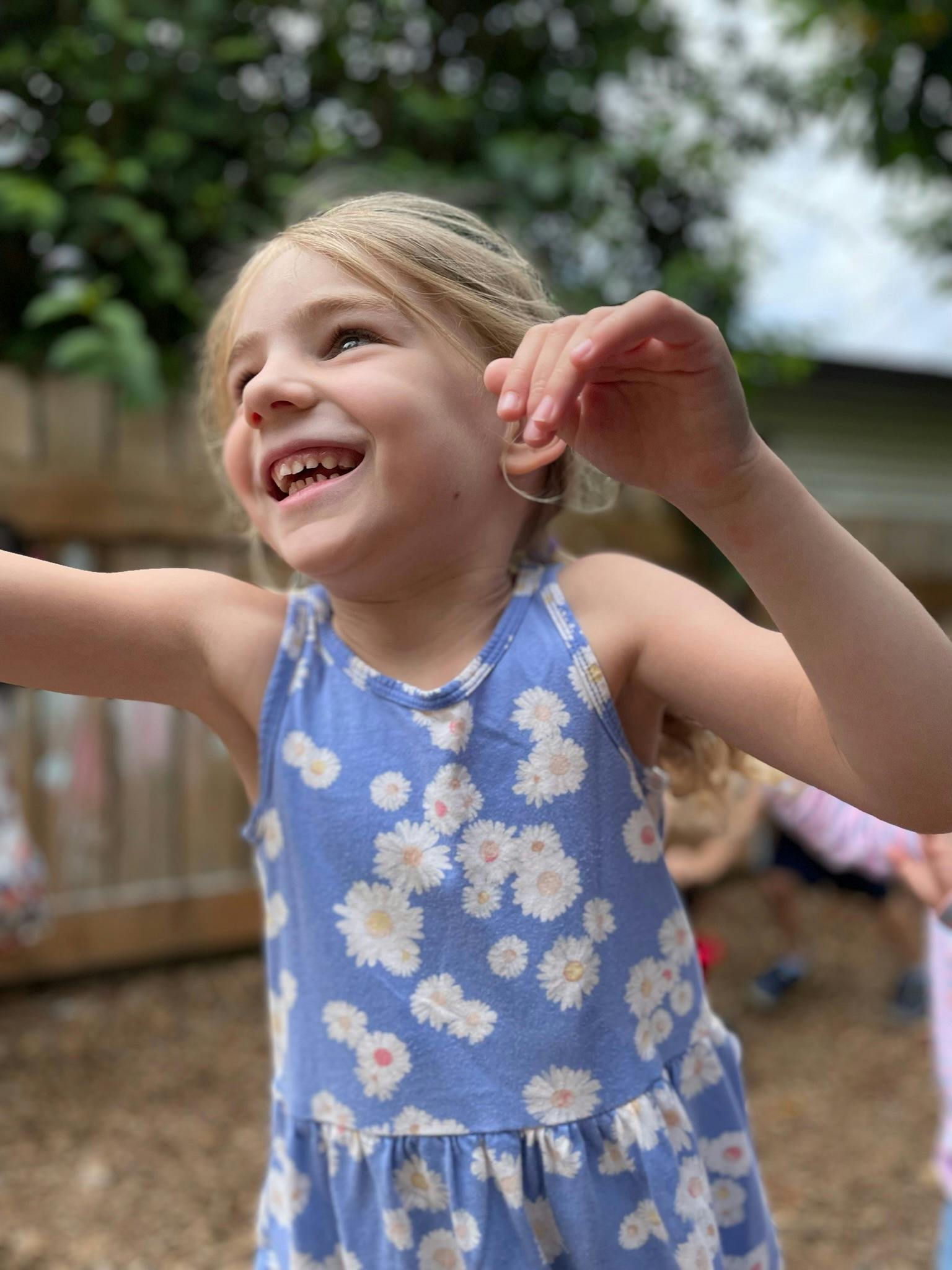 Child smiling with arms raised, wearing a blue floral dress