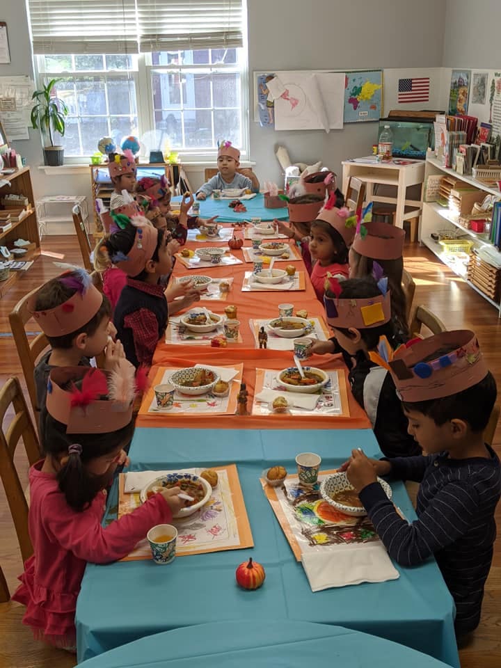 Children wearing paper hats eating at tables in a classroom