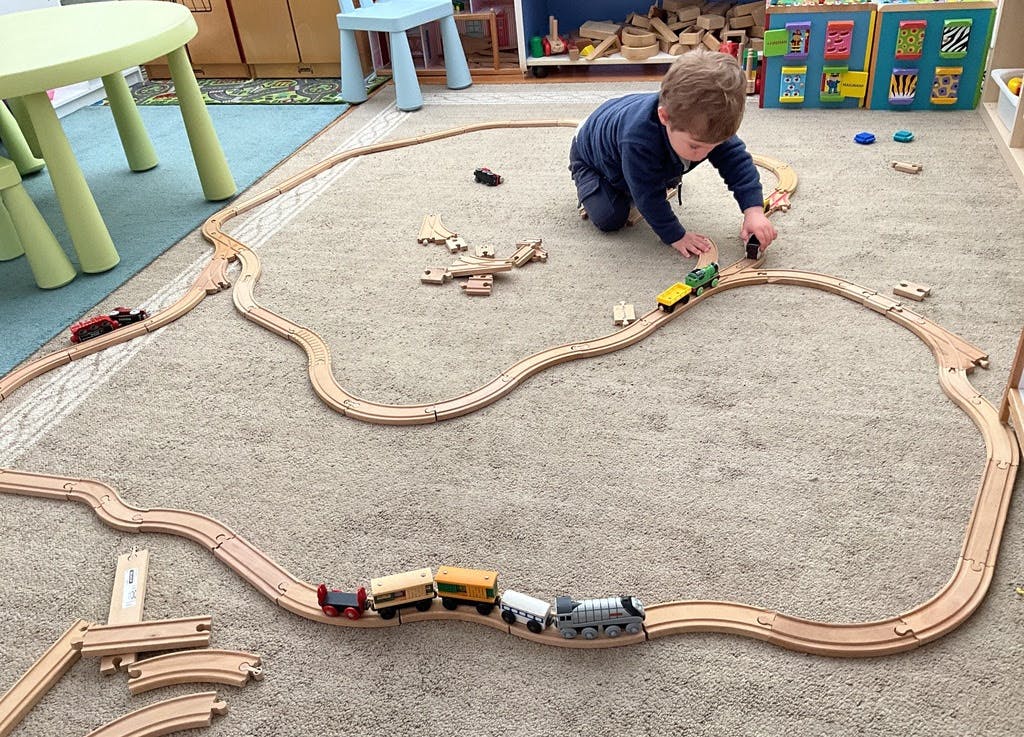 child playing with a wooden toy train set on a carpet