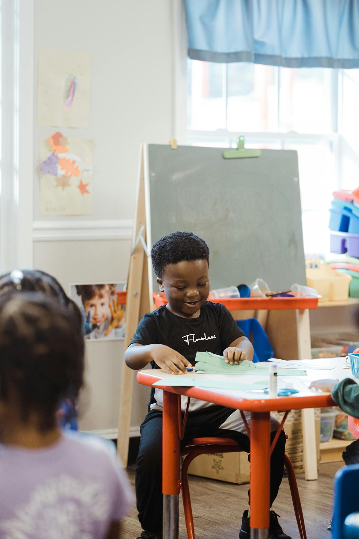 Child sitting at a table cutting paper in a classroom