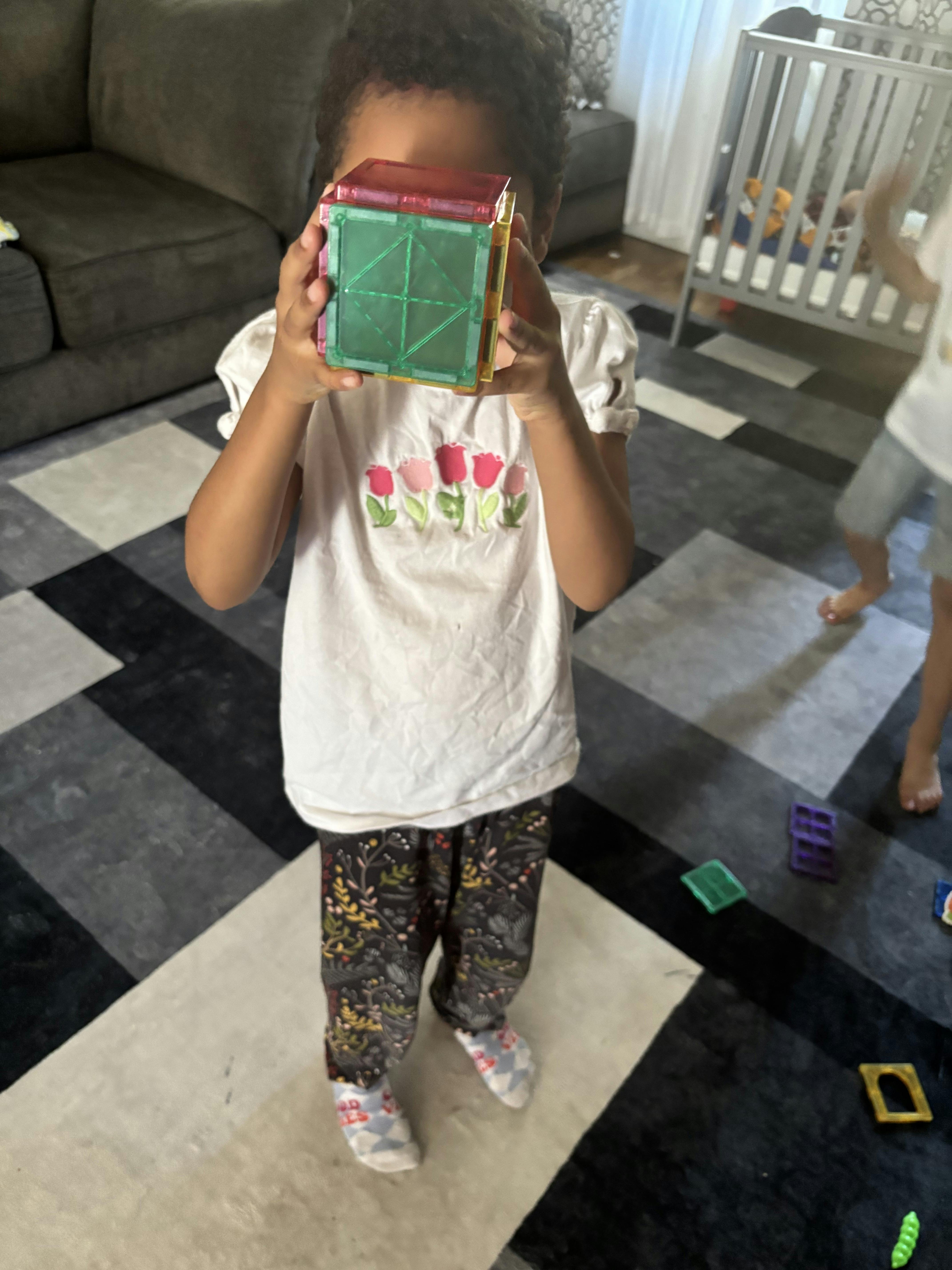 Child holding a magnetic building block in front of their face