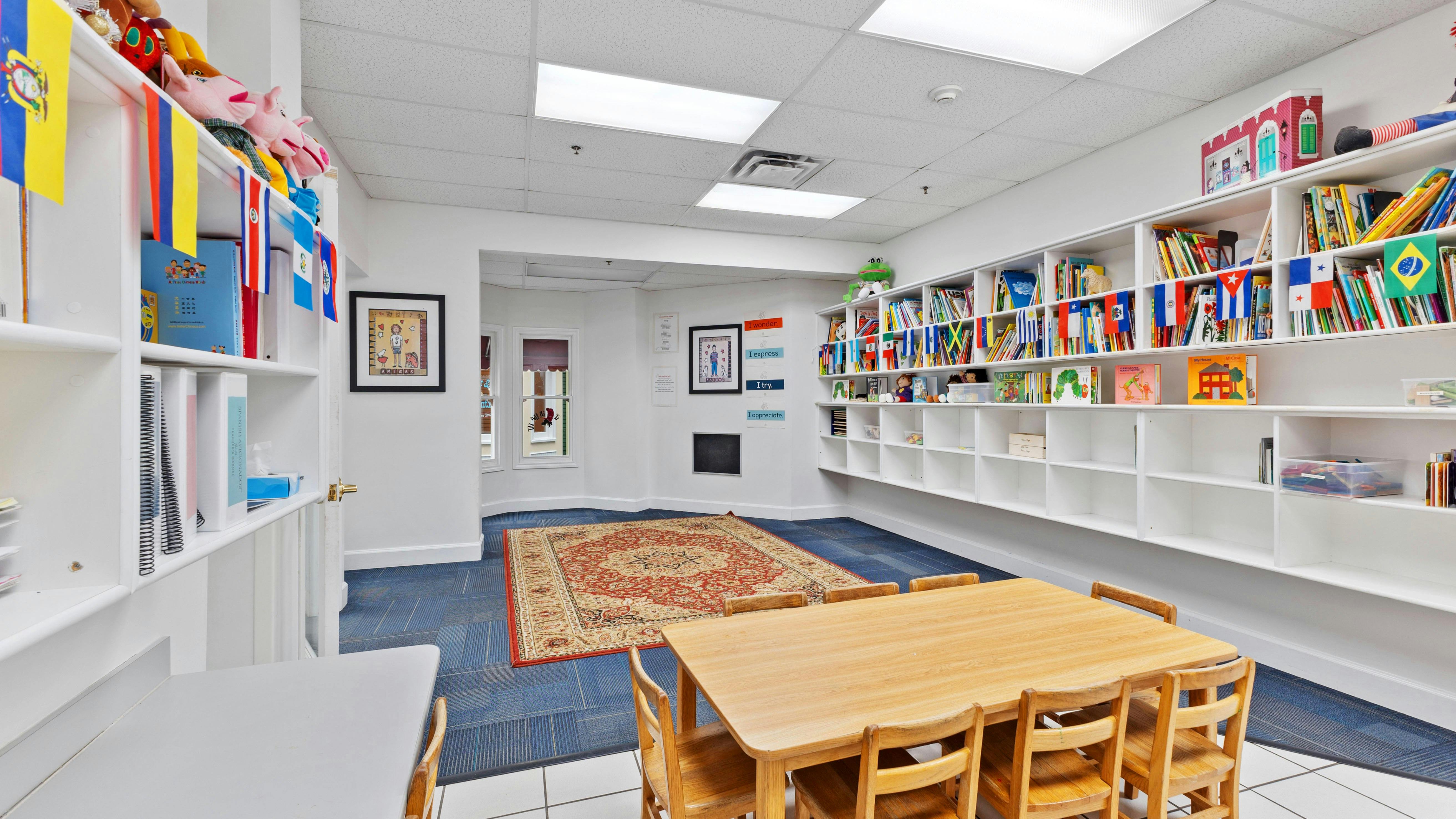 Children's classroom with small wooden tables and chairs, bookshelves with books and flags