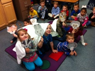 Children sitting on a rug holding up animal masks