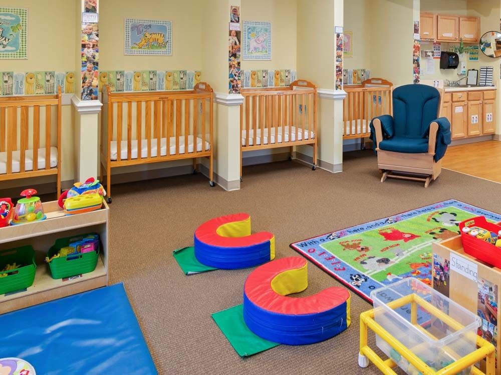 cribs in a nursery or daycare room with play mats and a rocking chair