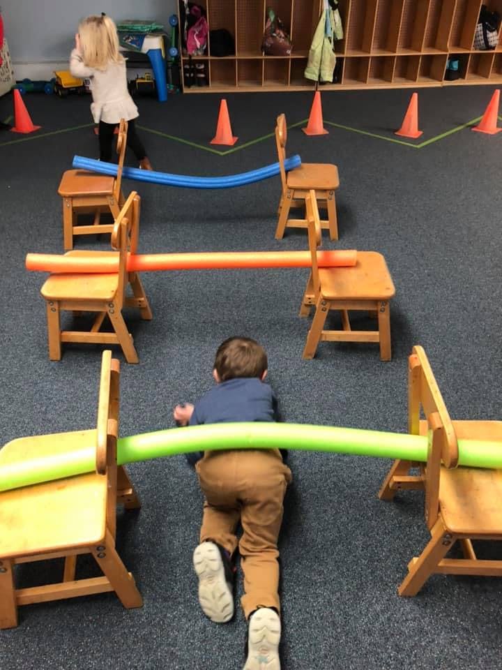 Child crawling under a pool noodle obstacle course in a classroom