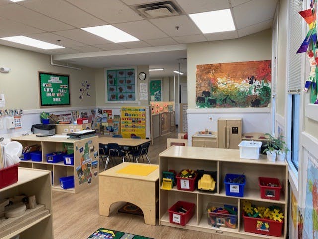 Classroom with child-sized furniture, art on walls, and toy storage shelves