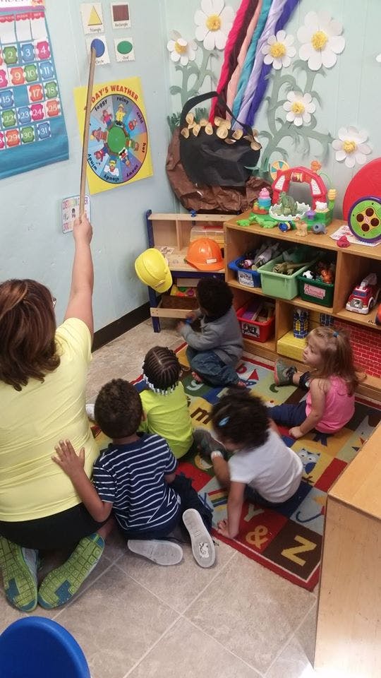 Person pointing to a chart with children sitting on a rug in a classroom