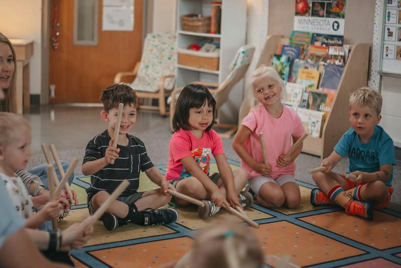 Group of children sitting on a classroom rug playing with wooden rhythm sticks