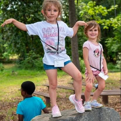 Three children playing outdoors, two standing on a rock