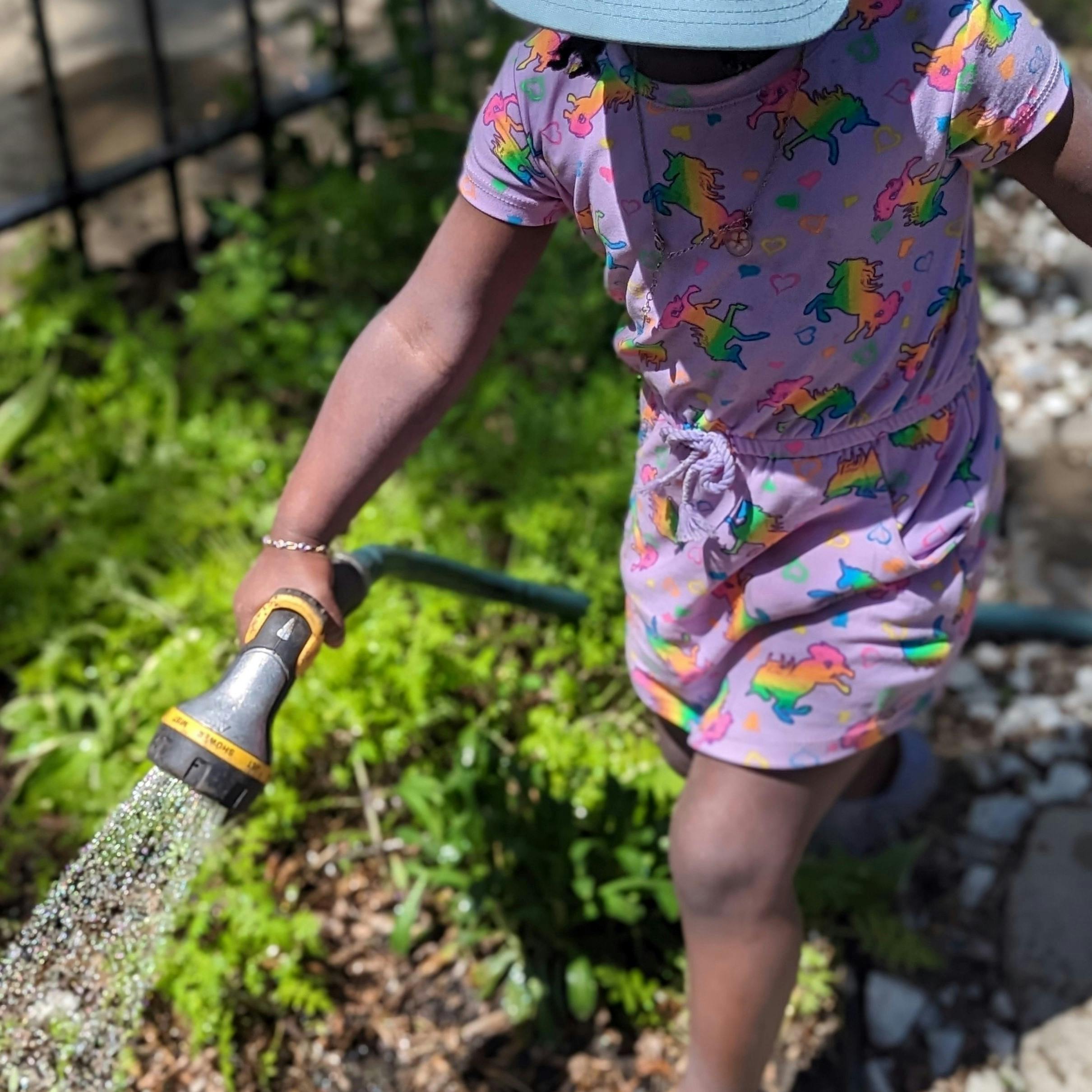 Child watering plants with a hose