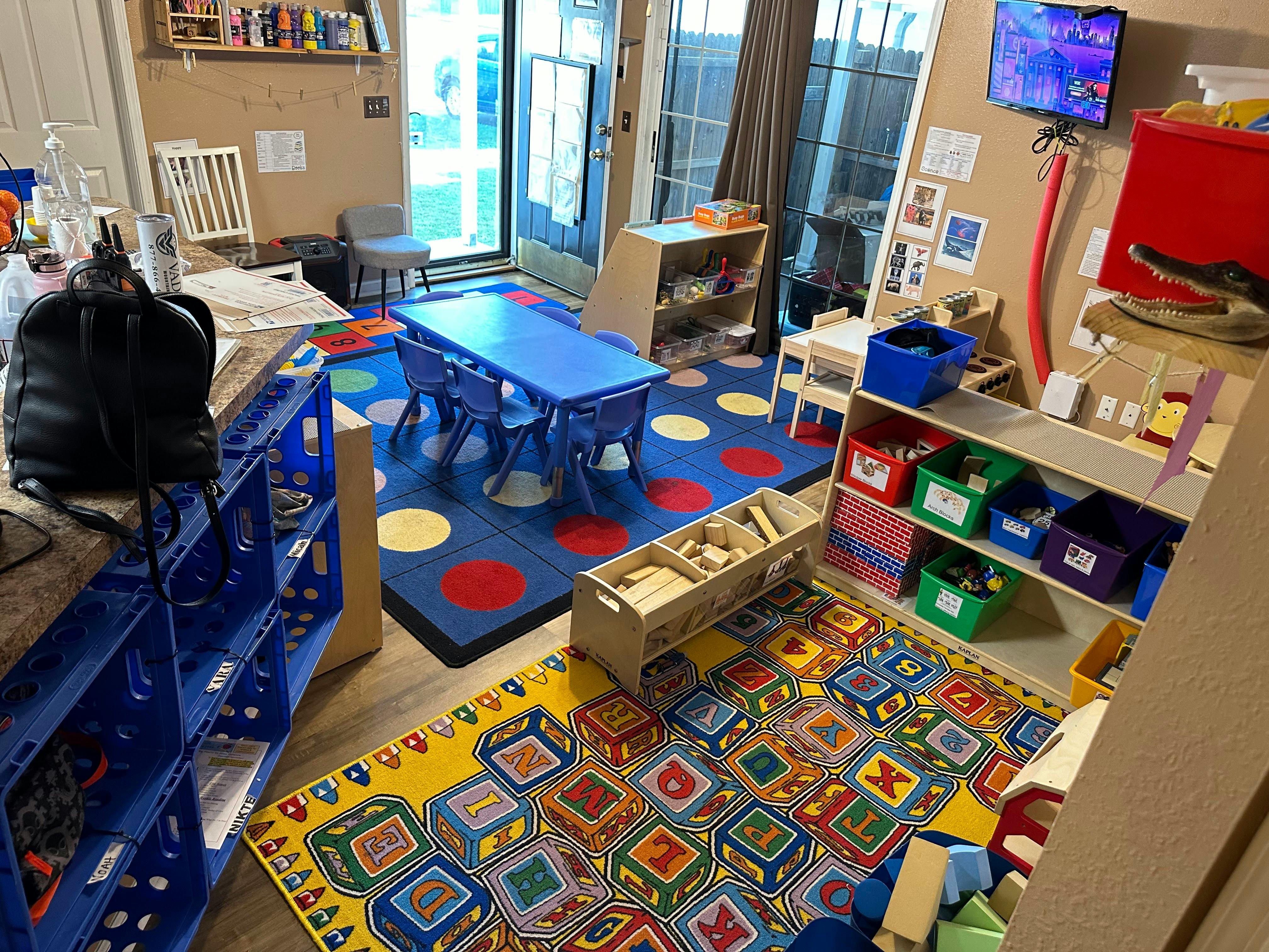 Playroom with blue table and chairs, colorful rugs, and shelves with toys