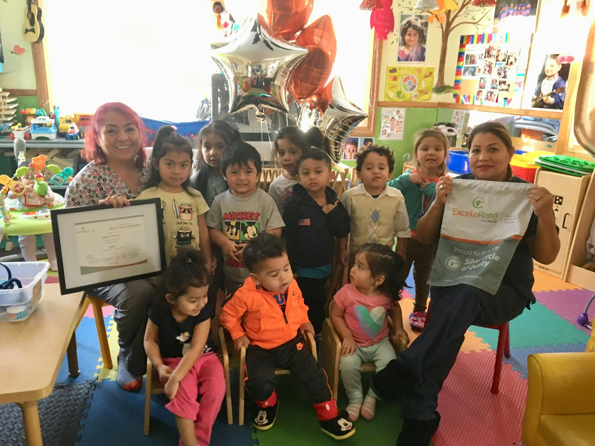 Two people and multiple children in a classroom holding certificates