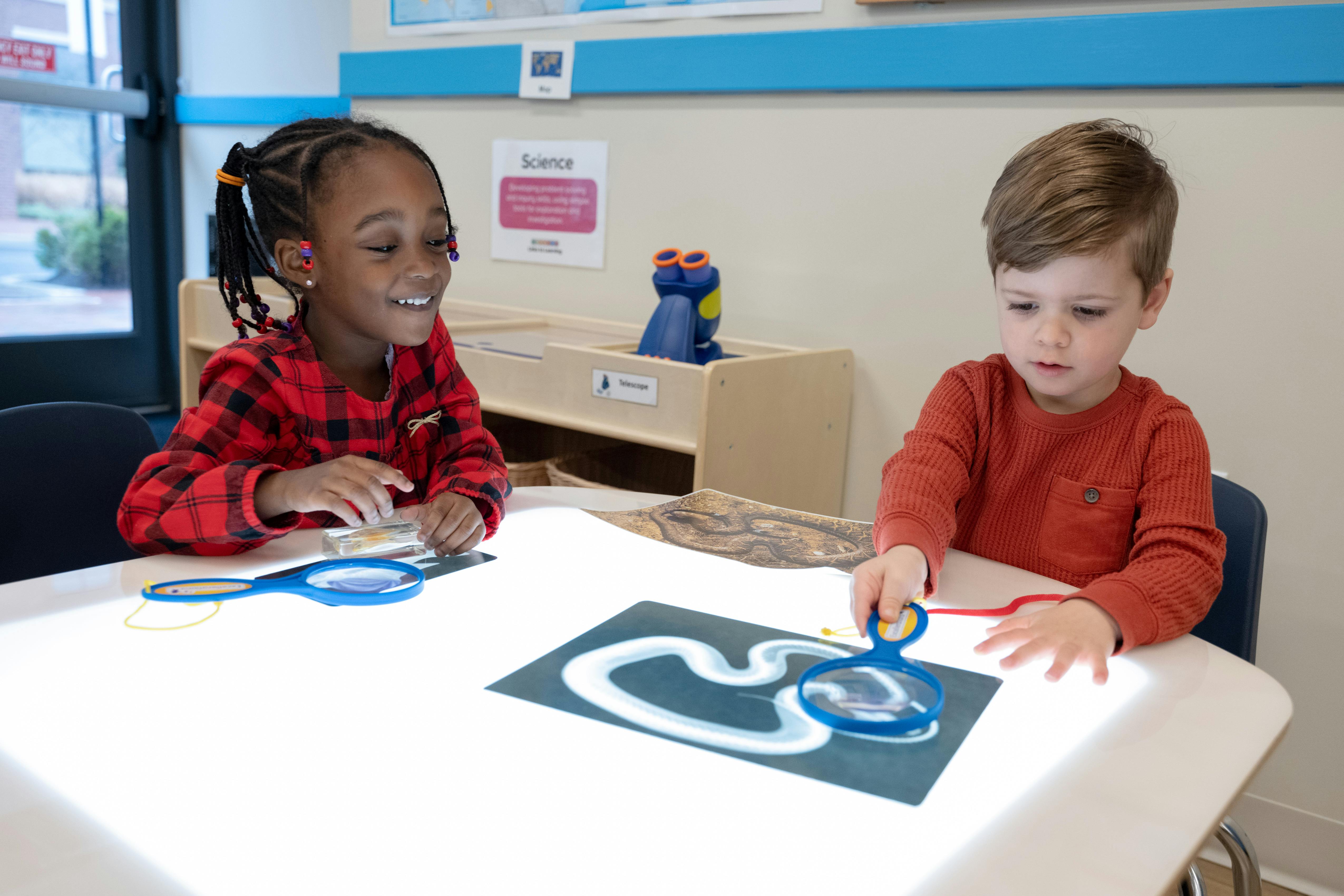 Two children at a table with magnifiers and a light board