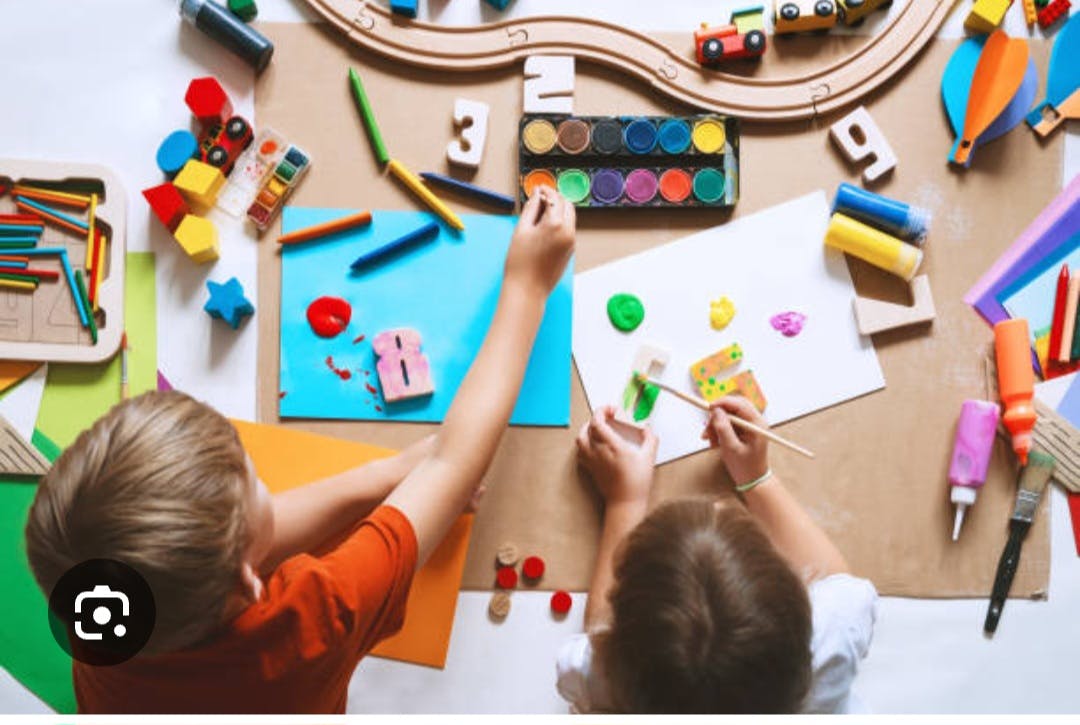 Two children painting and coloring at a table with art supplies and toys