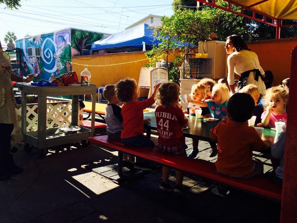 Children sitting at a table with an adult standing nearby