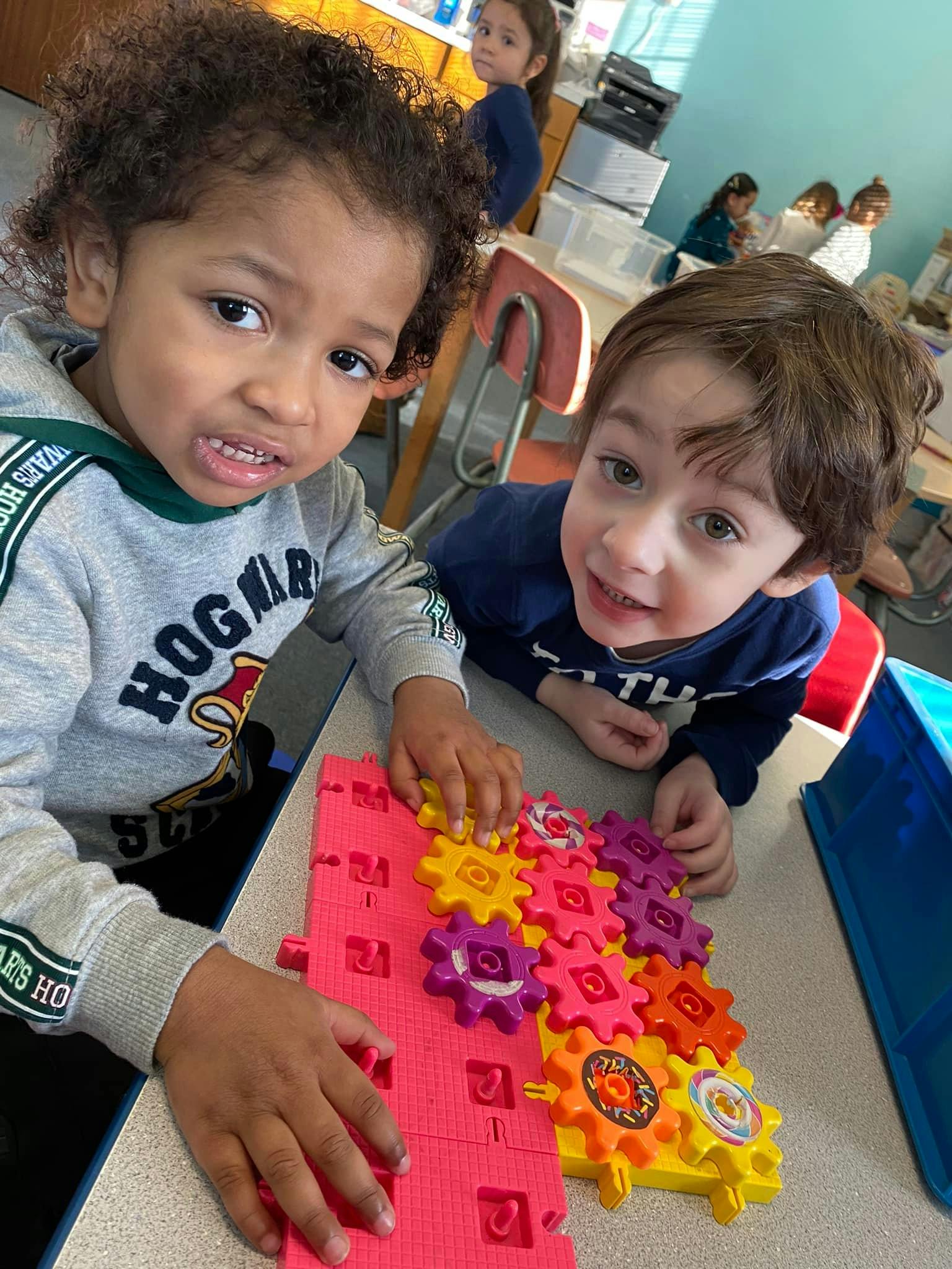 Two children playing with colorful interlocking gears on a table