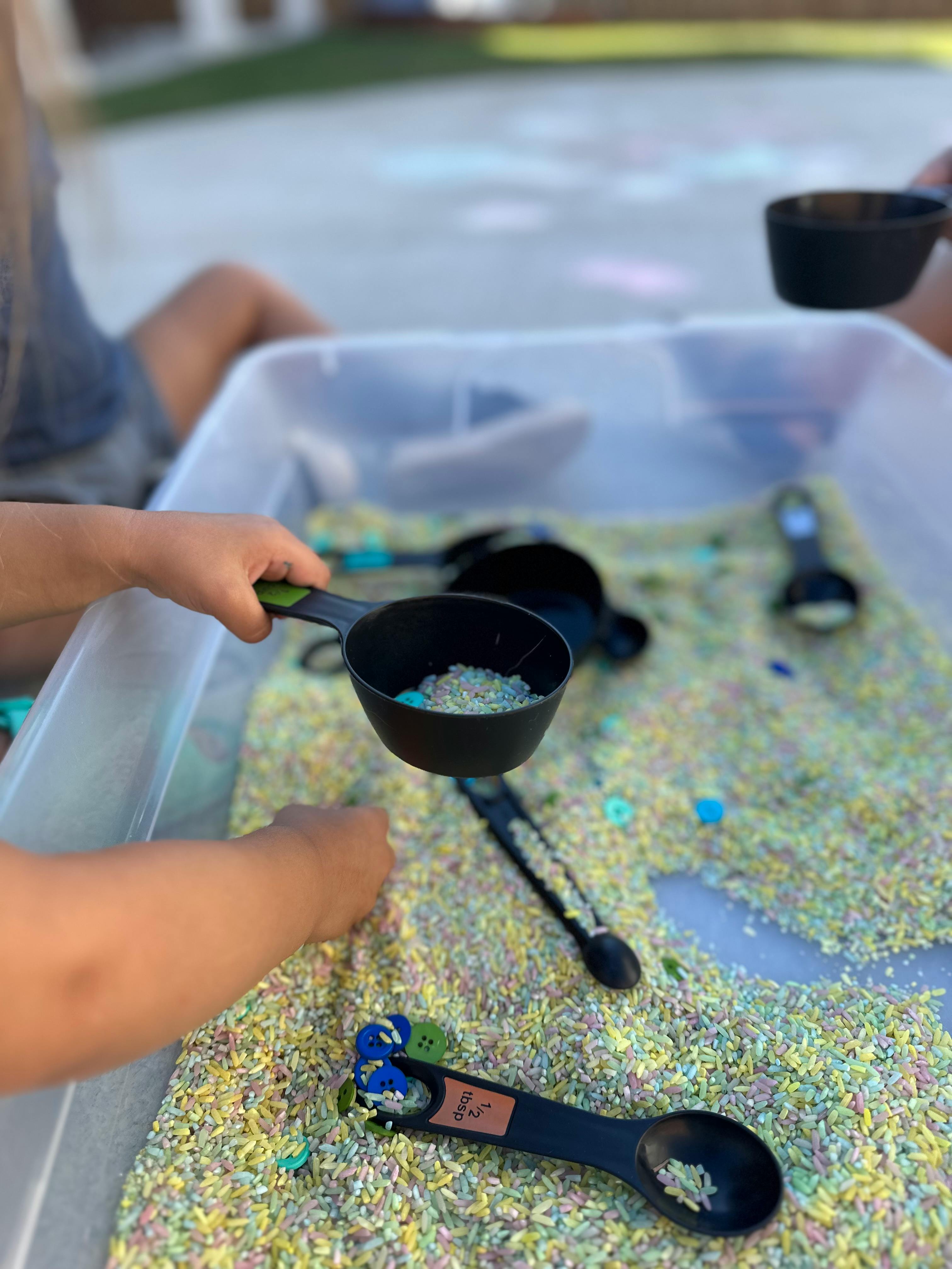 Child's hand holding a measuring cup filled with rice over a bin of rice