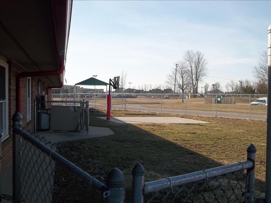Basketball hoop with a court next to a building and fenced yard