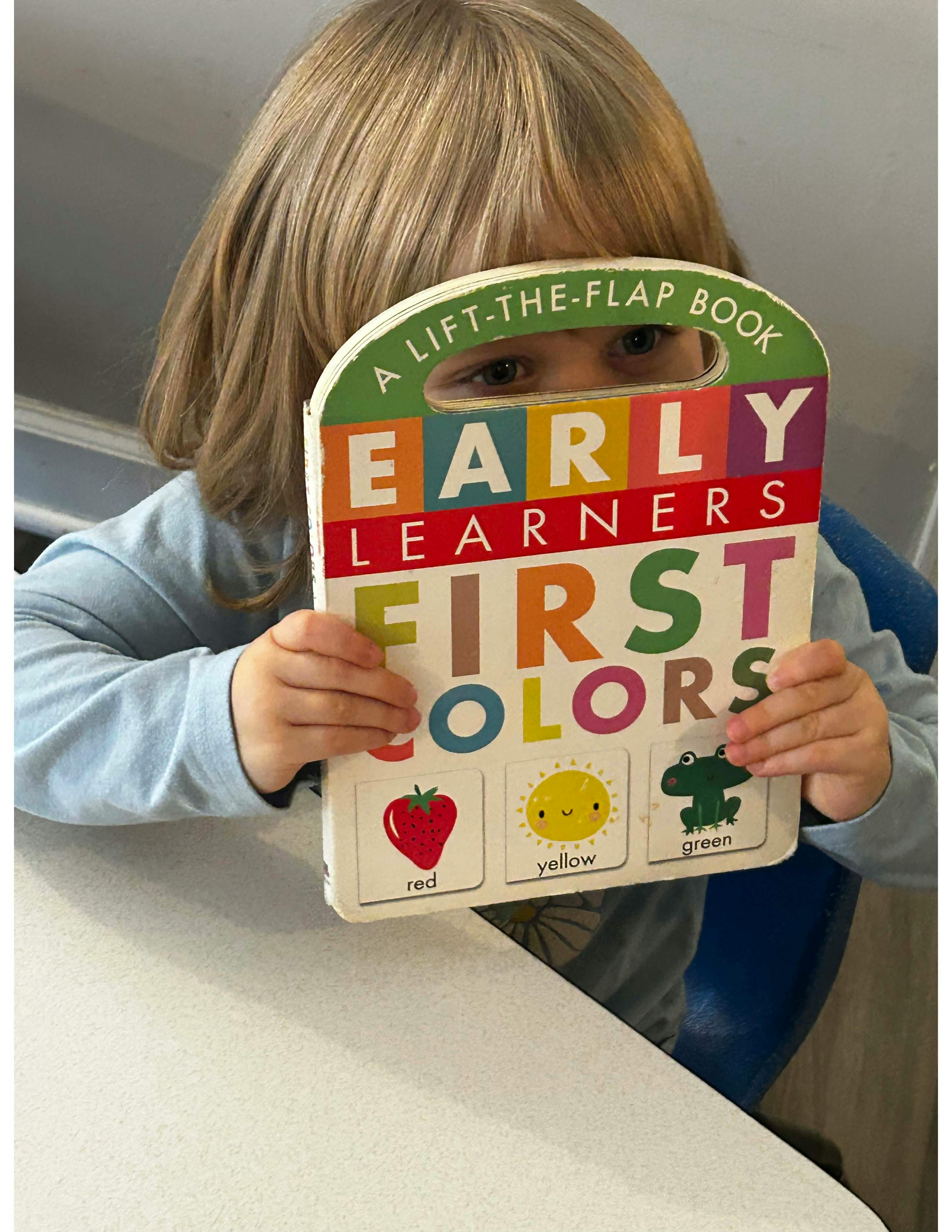 Child holding a lift-the-flap book titled "Early Learners First Colors"