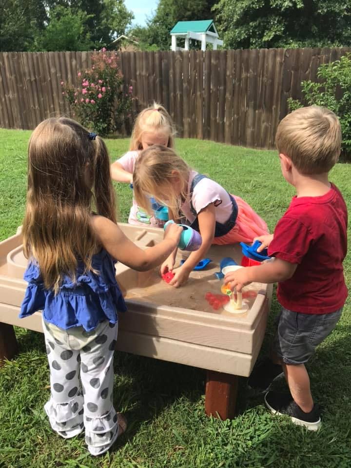 Four children playing in a sand and water table outdoors