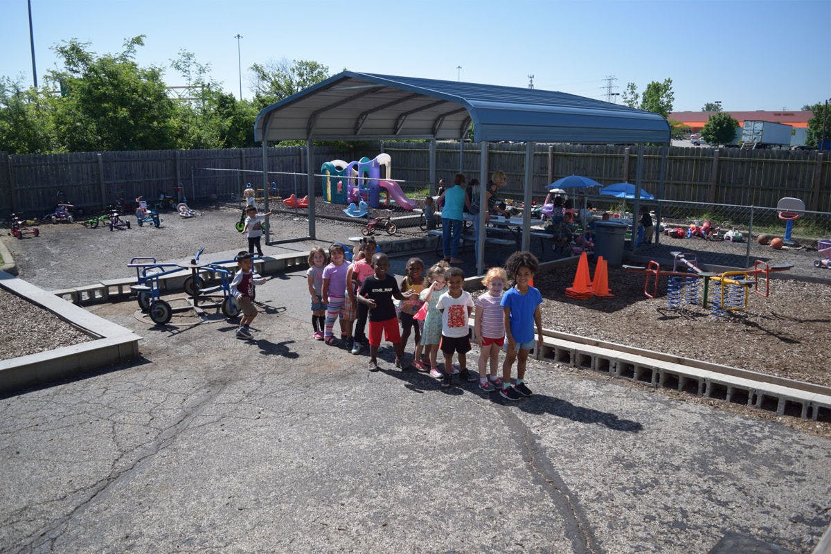 Children standing in a line on a paved area next to a playground