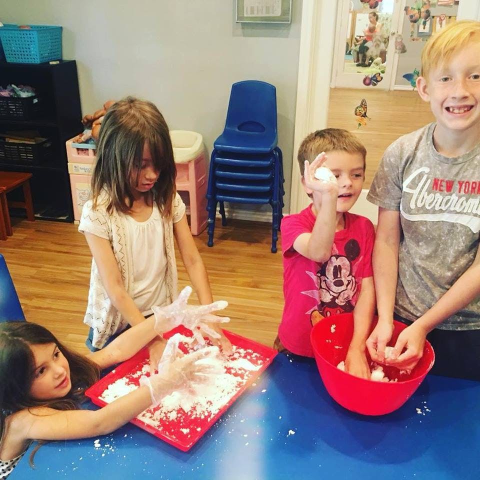 Children playing with white powdery substance in red trays and bowls