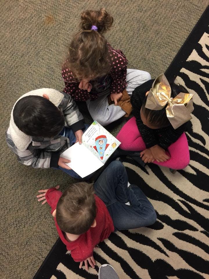 Four children sitting on a carpet, one holding an open book