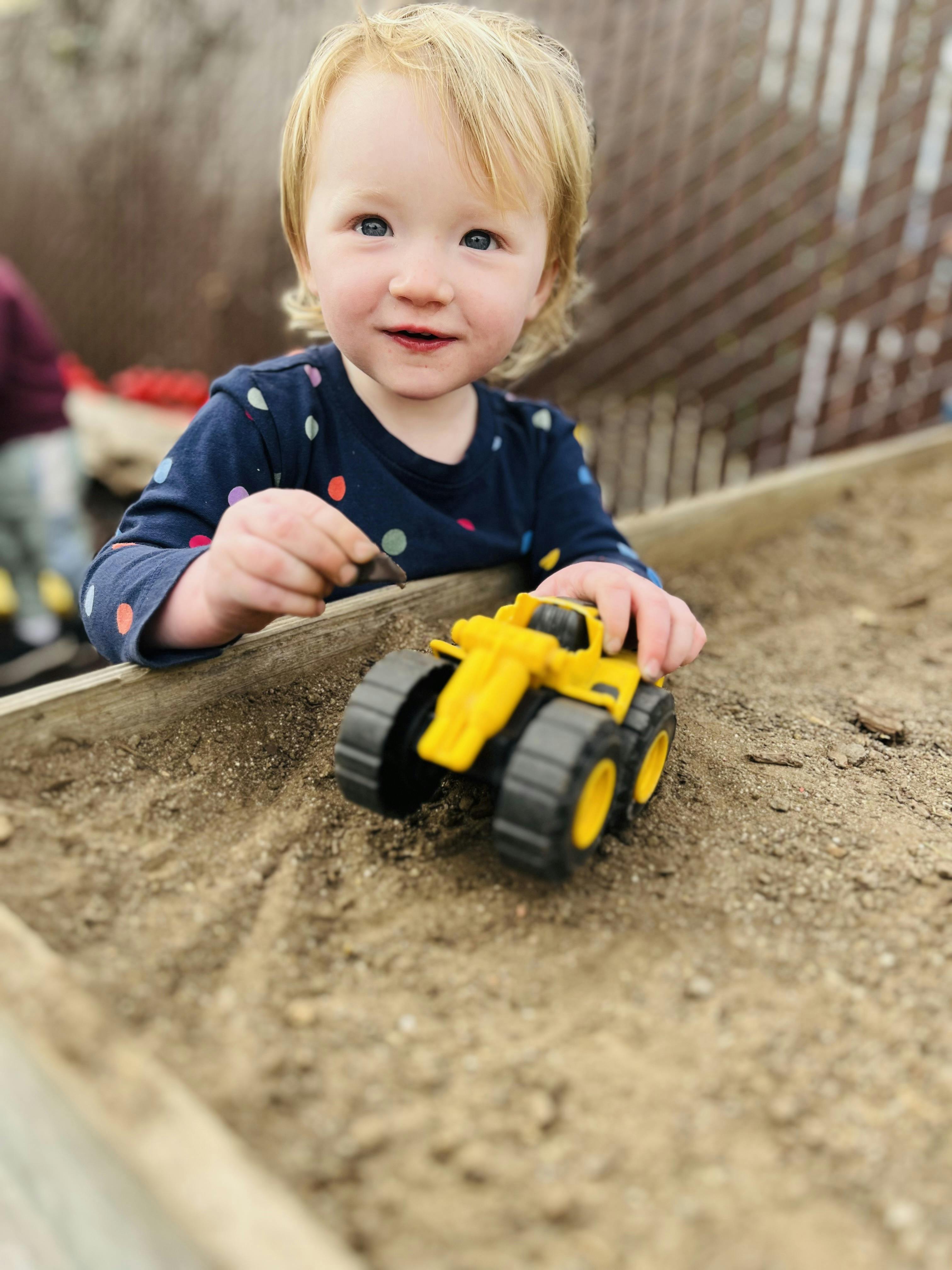 Child playing in sand with a yellow toy truck