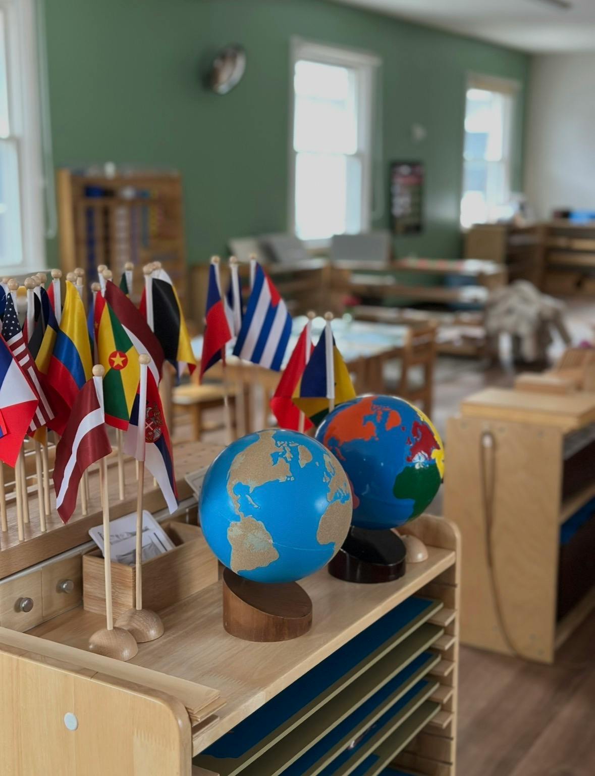 Small international flags and two globes on a wooden shelf in a classroom