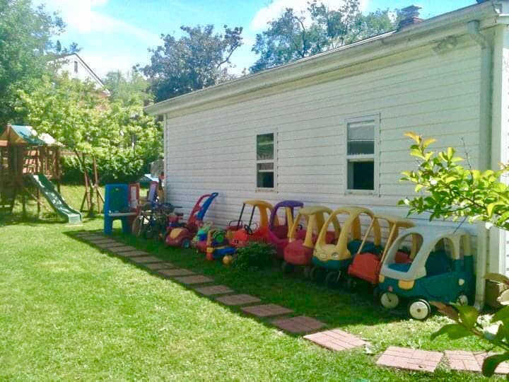 Children's ride-on toys lined up against a white building with a playground