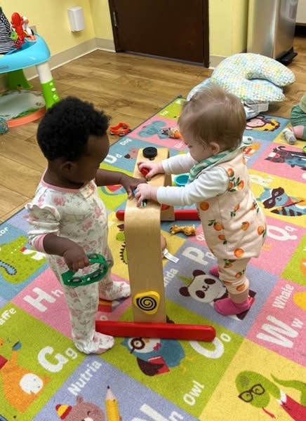 Two children playing with a wooden activity toy on a colorful mat