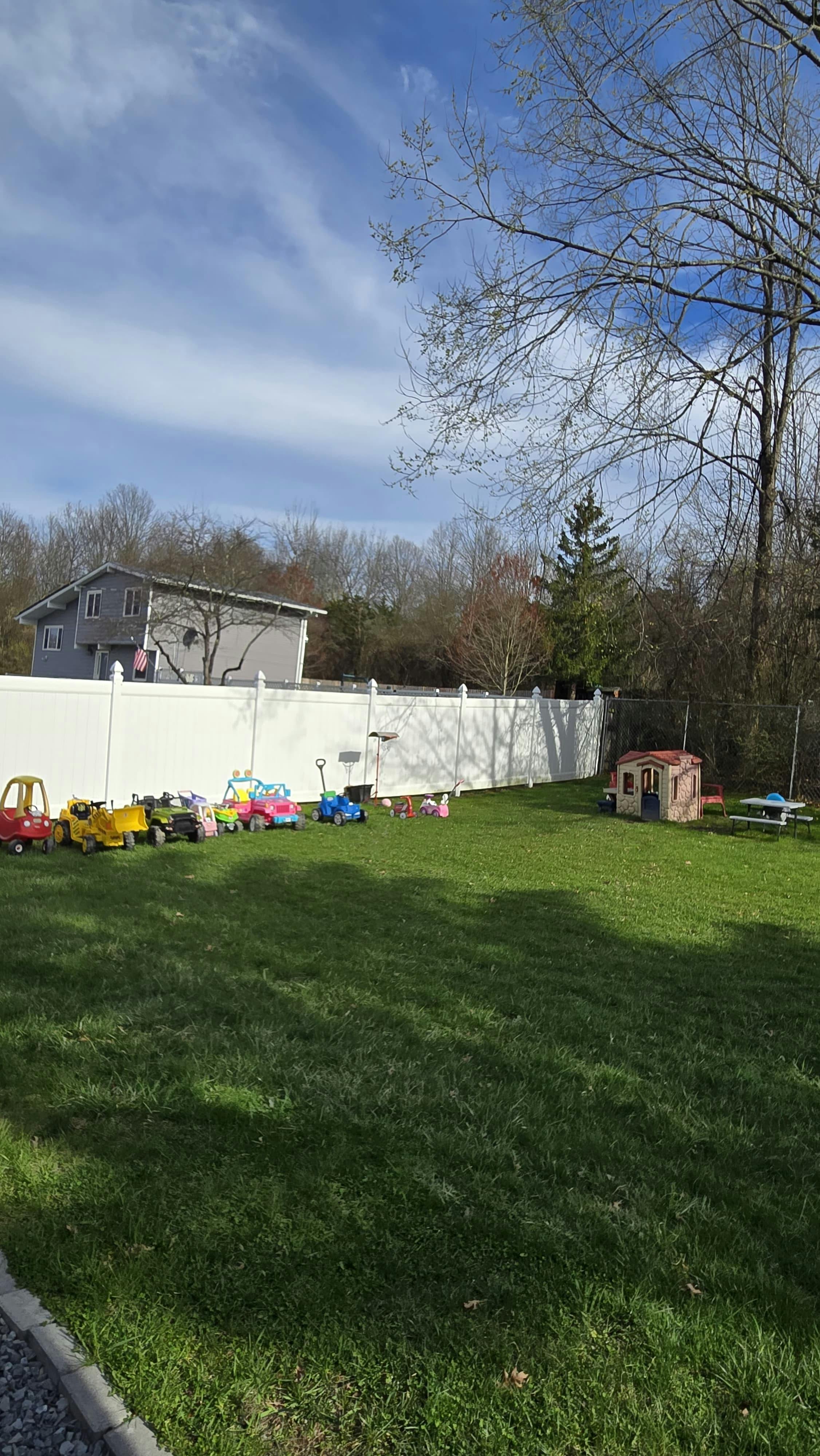 Playground with several toy cars, a playhouse, and a picnic table on grass