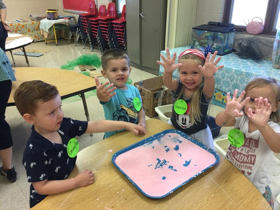 Four children with hands covered in paint around a table