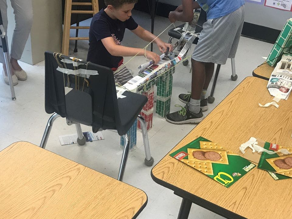 Child working on a craft project with another person standing nearby