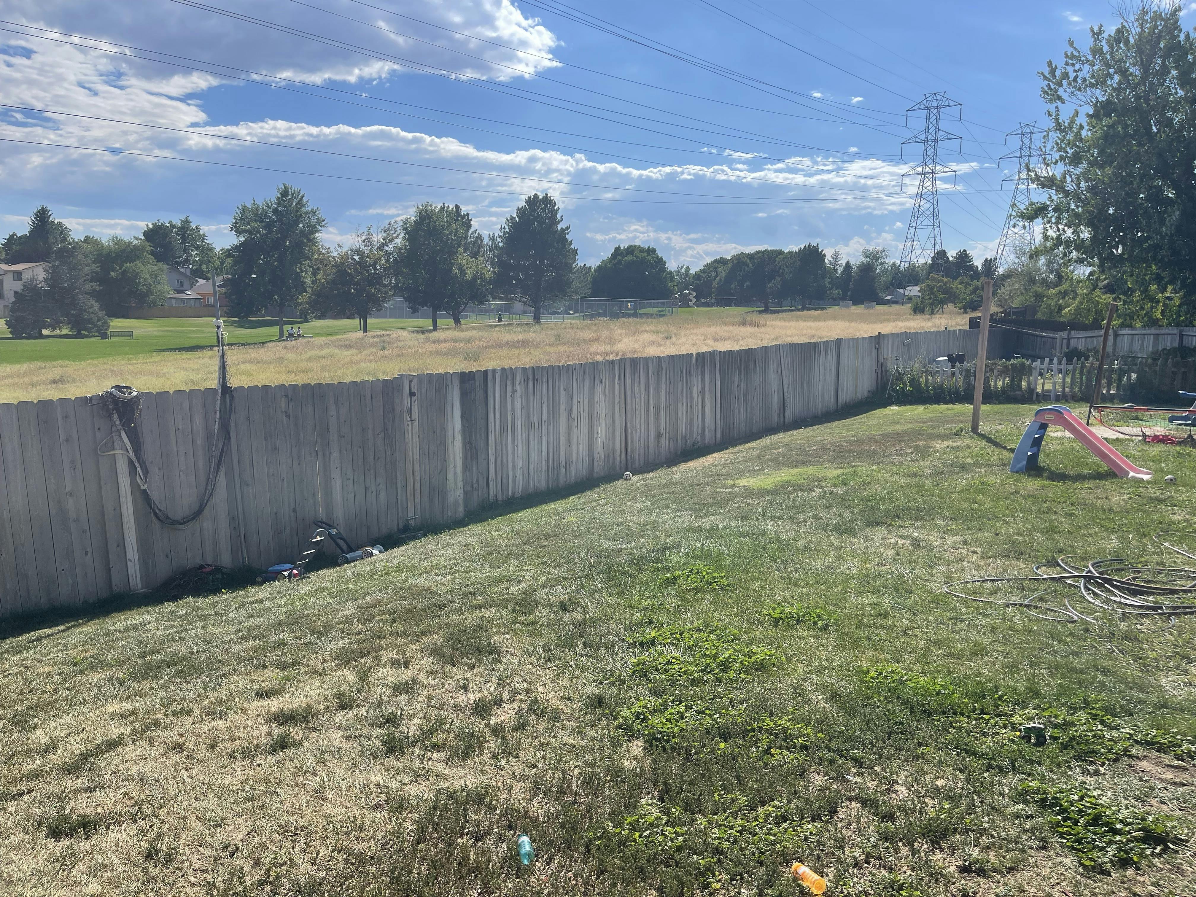Backyard with a wooden fence and a grassy field beyond