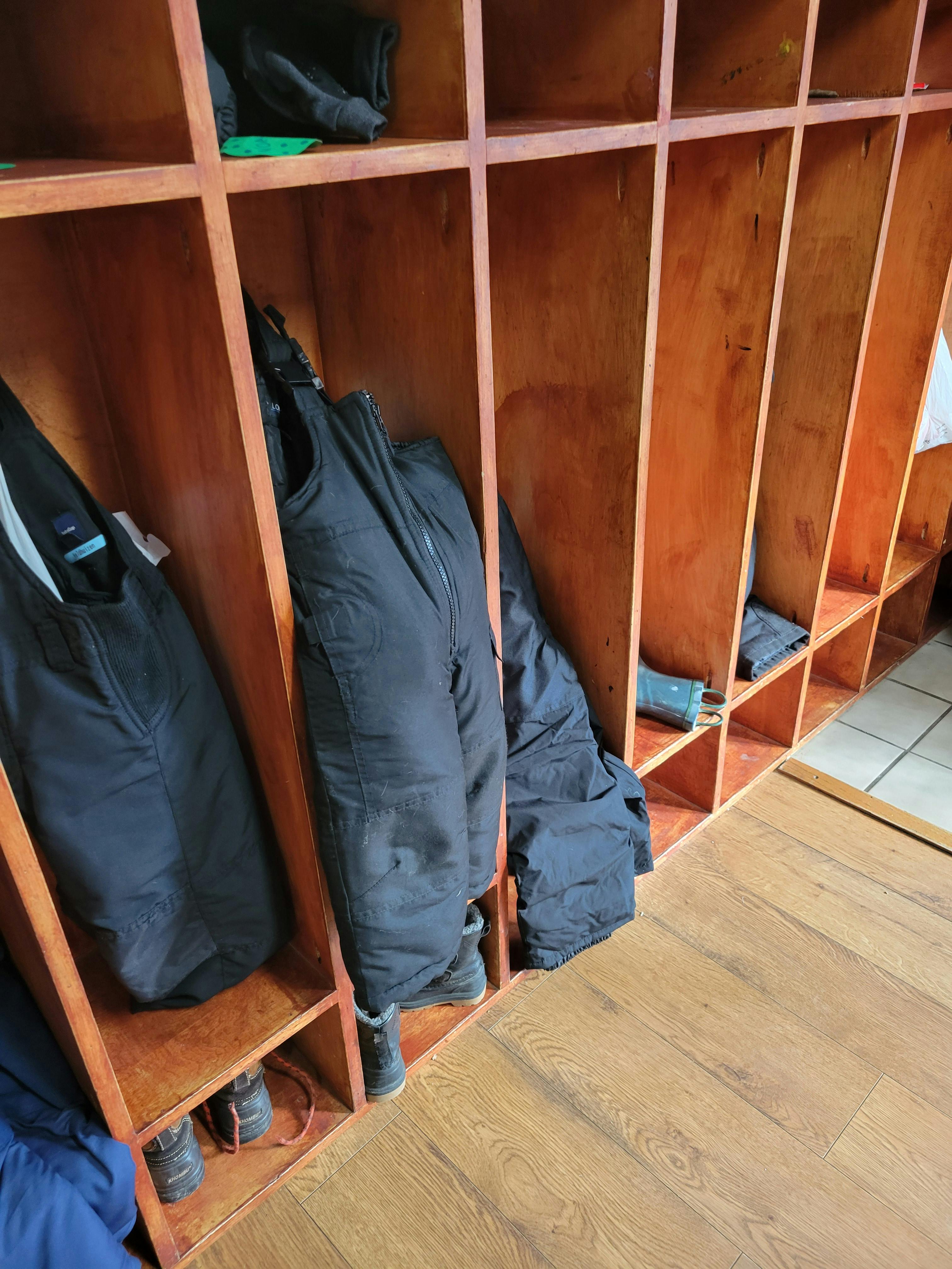 Black winter clothing and boots in wooden cubbies