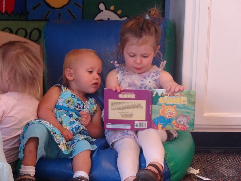 Two children sitting on a blue and green soft play structure, one holding books