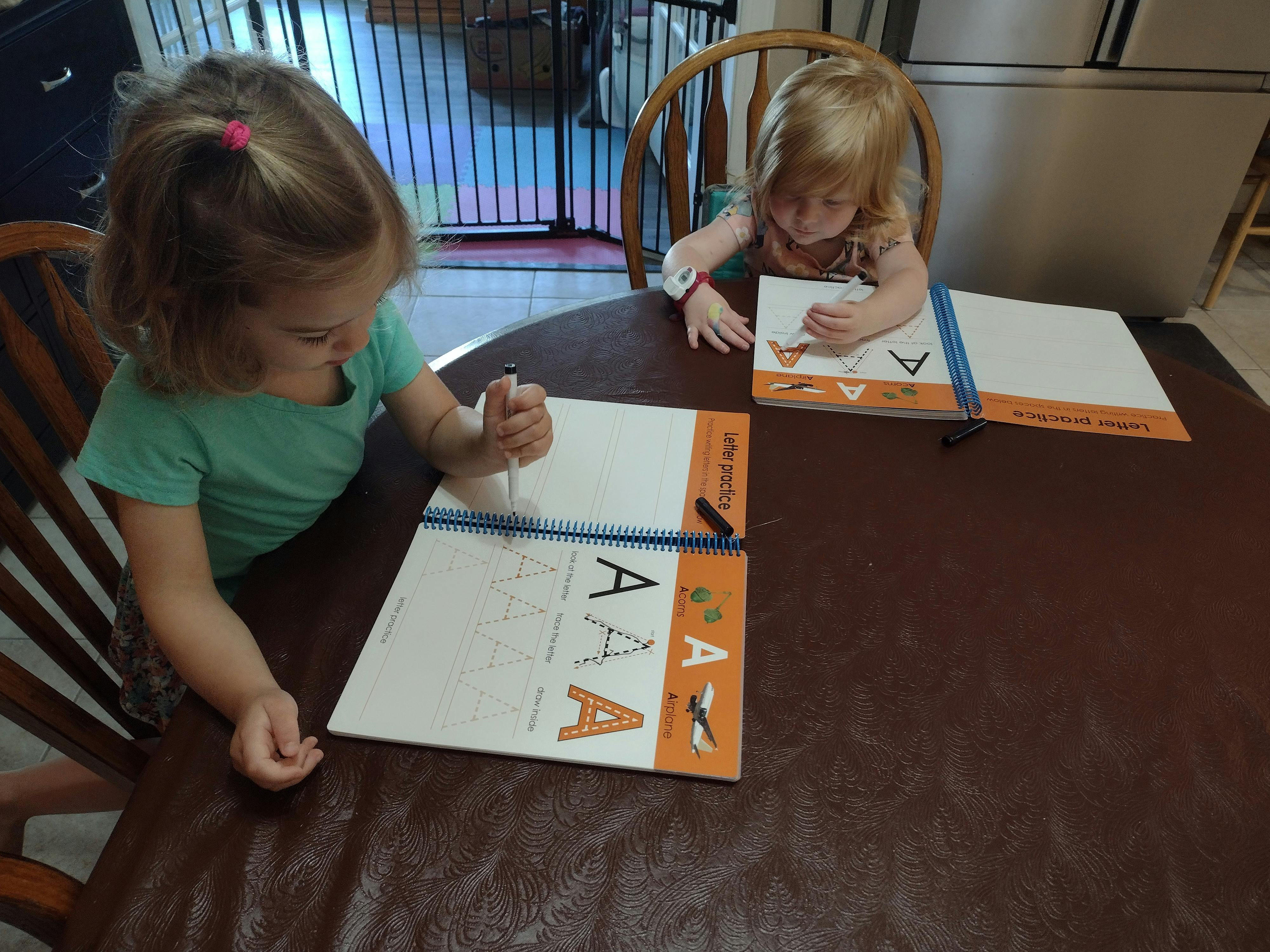 Two children writing in workbooks at a table