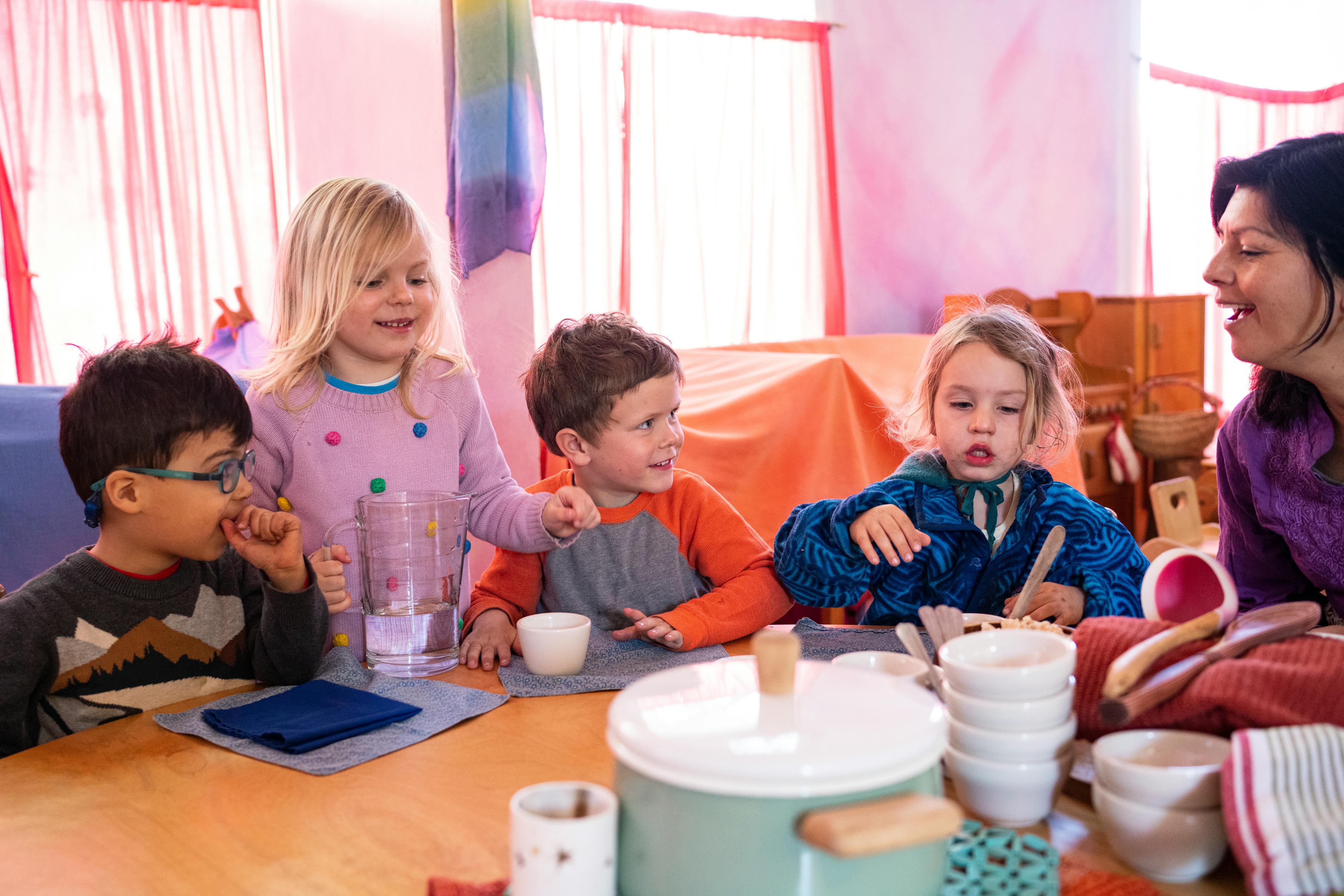 Four children and one adult sitting at a table with dishes