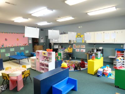 Classroom with tables, chairs, and toys, with a person sitting in the background