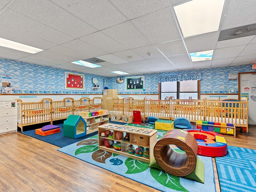 A colorful daycare room with several wooden cribs and play mats