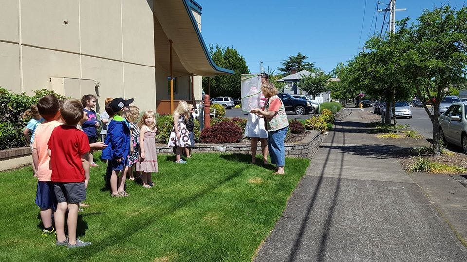 Adult and children gathered on grass next to a building