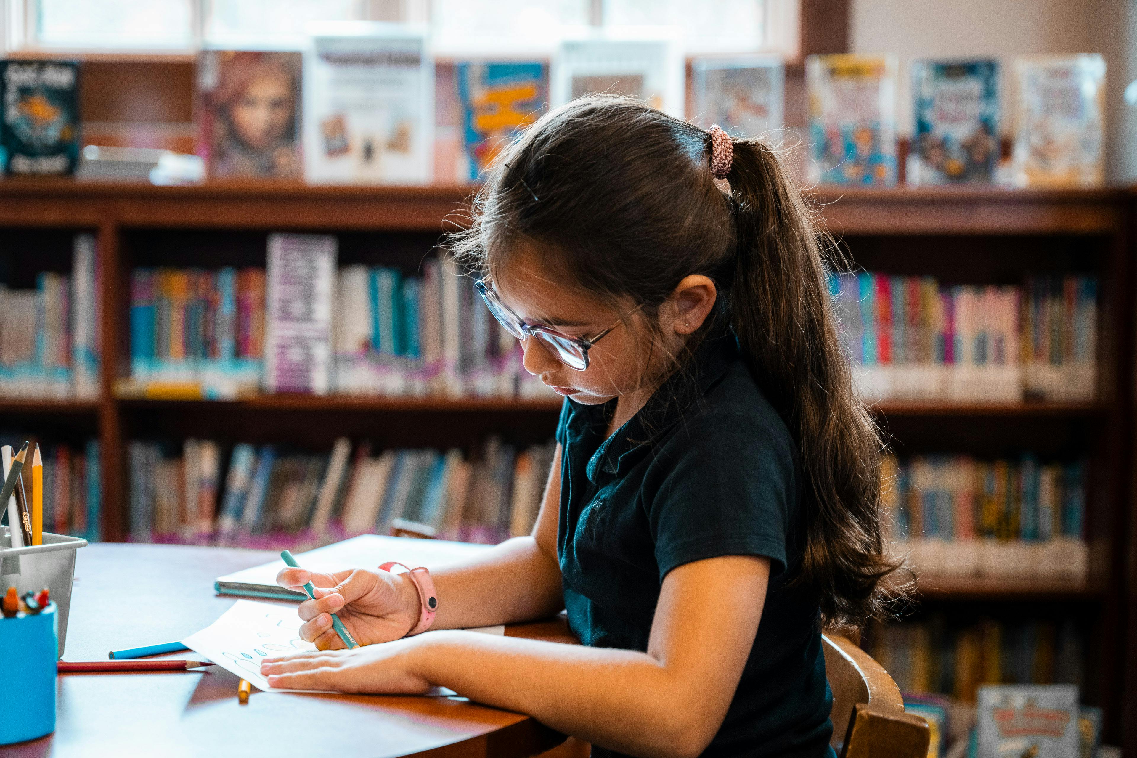 Child with glasses coloring at a table in a library