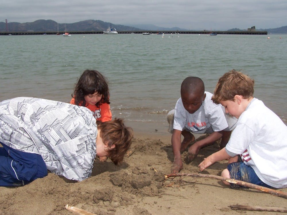 Four children playing in sand on a beach next to water